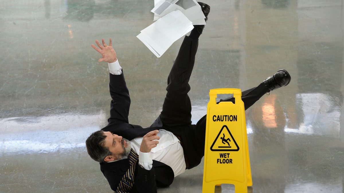 Businessman-slipping-beside-wet-floor-sign-indoors