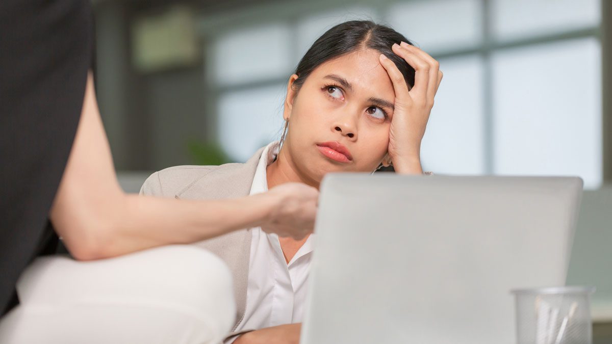 Frustrated employee listening to colleague while working on laptop