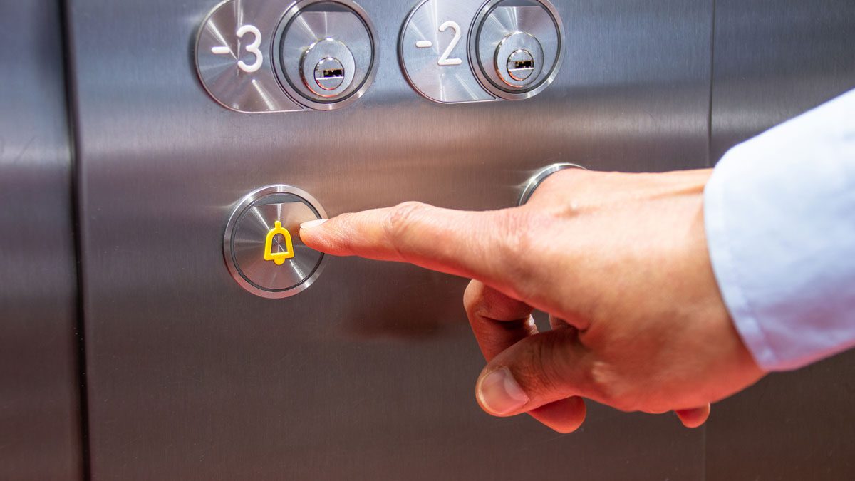 Hand pressing elevator alarm button inside lift panel