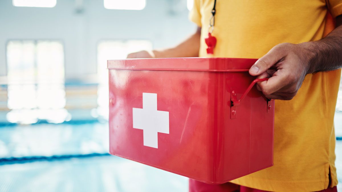 Lifeguard holding red first aid kit by pool