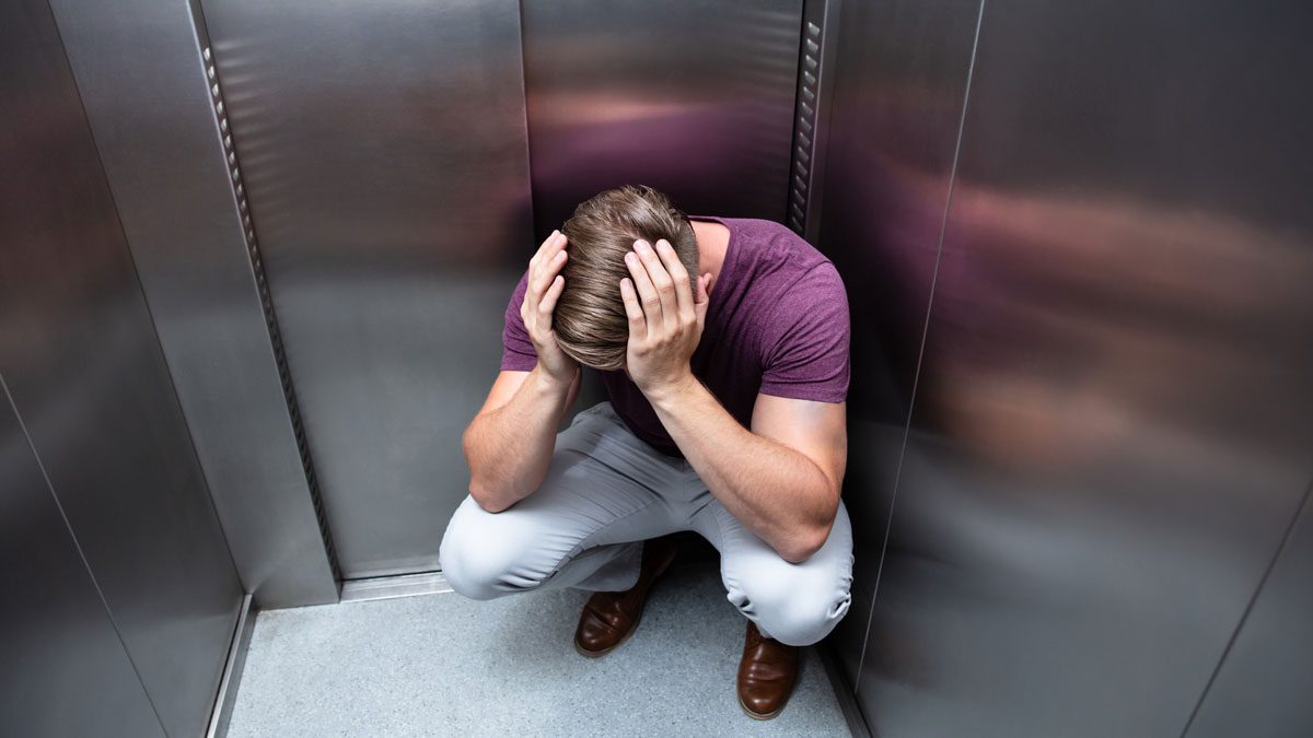 Man crouching in elevator holding head during stressful situation