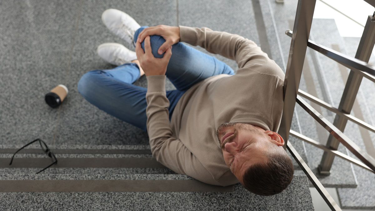 Man seated on stairs clutching injured knee