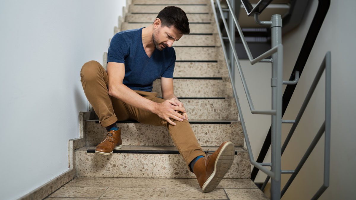 Man sitting on stairs holding painful knee