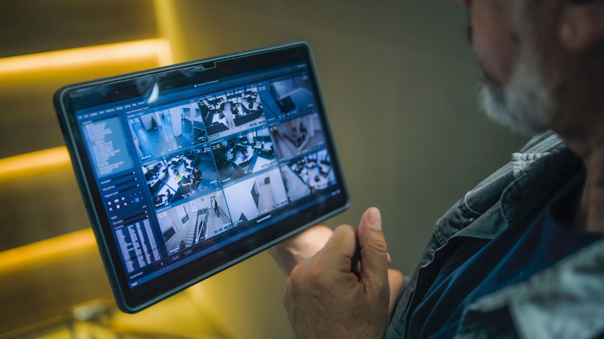 Person monitoring multiple security camera feeds on digital tablet