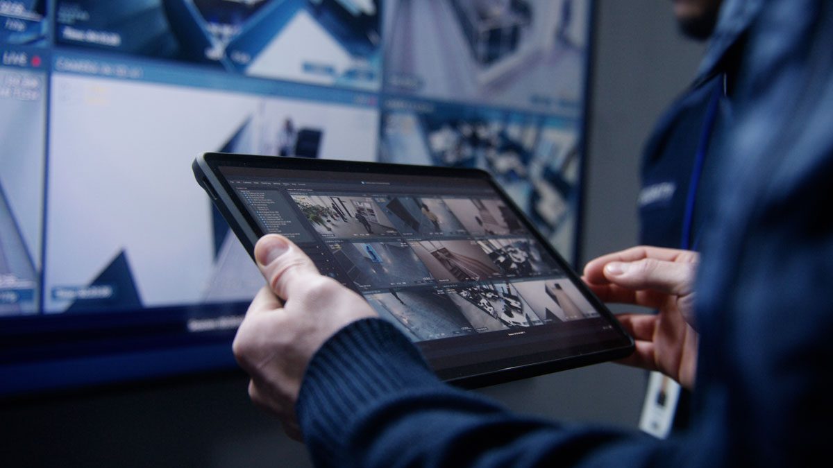 Person monitoring security cameras on digital tablet