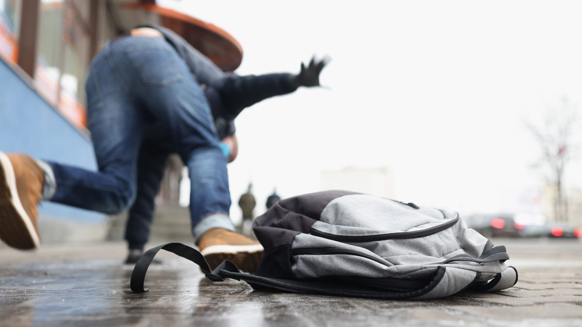 Person slipping on wet sidewalk with bag in foreground