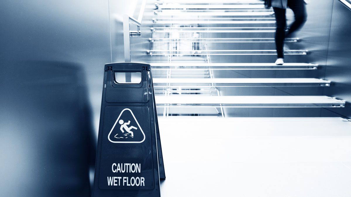 Wet floor sign beside staircase with person walking up