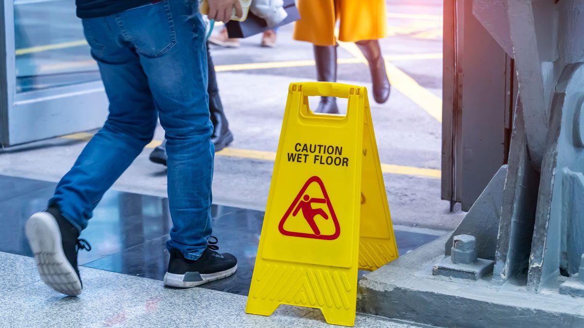 Wet floor sign near doorway with pedestrians passing
