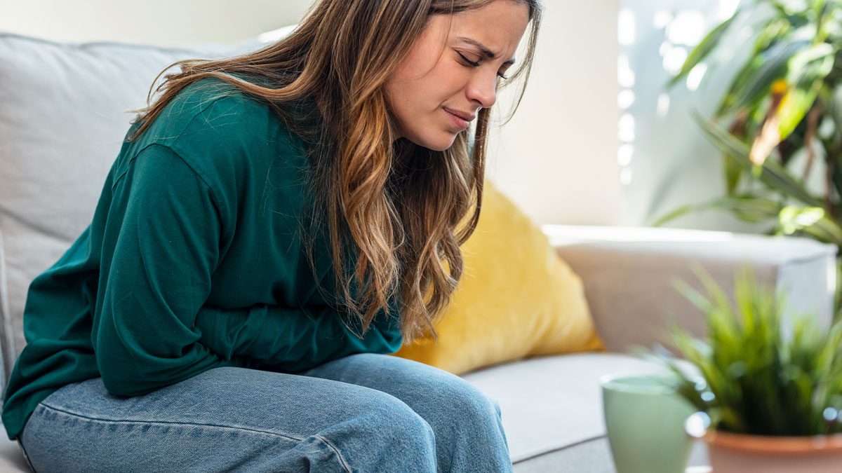 Woman sitting on couch holding abdomen in pain