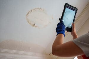 person-photographing-a-water-stained-ceiling-with-a-tablet